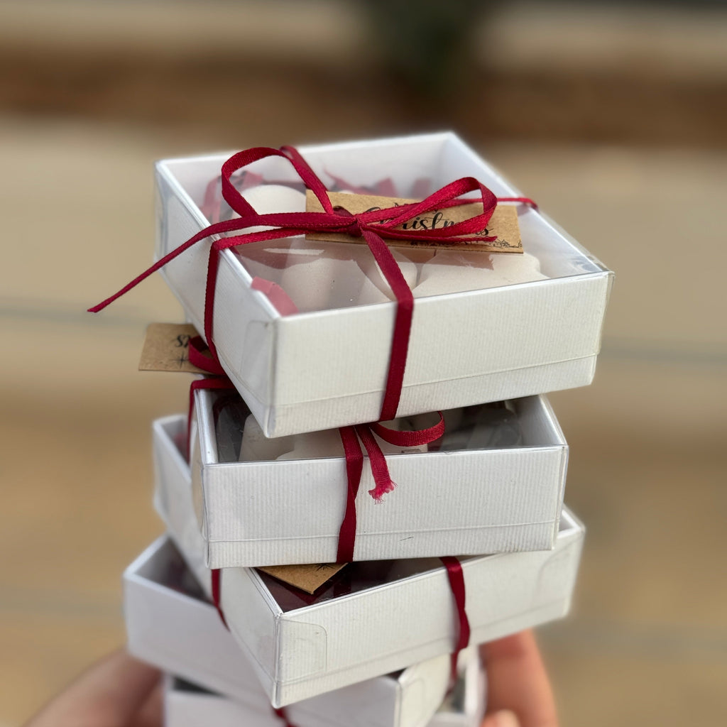 Stack of white Christmas gift boxes tied with red ribbons held by a hand against a blurred background