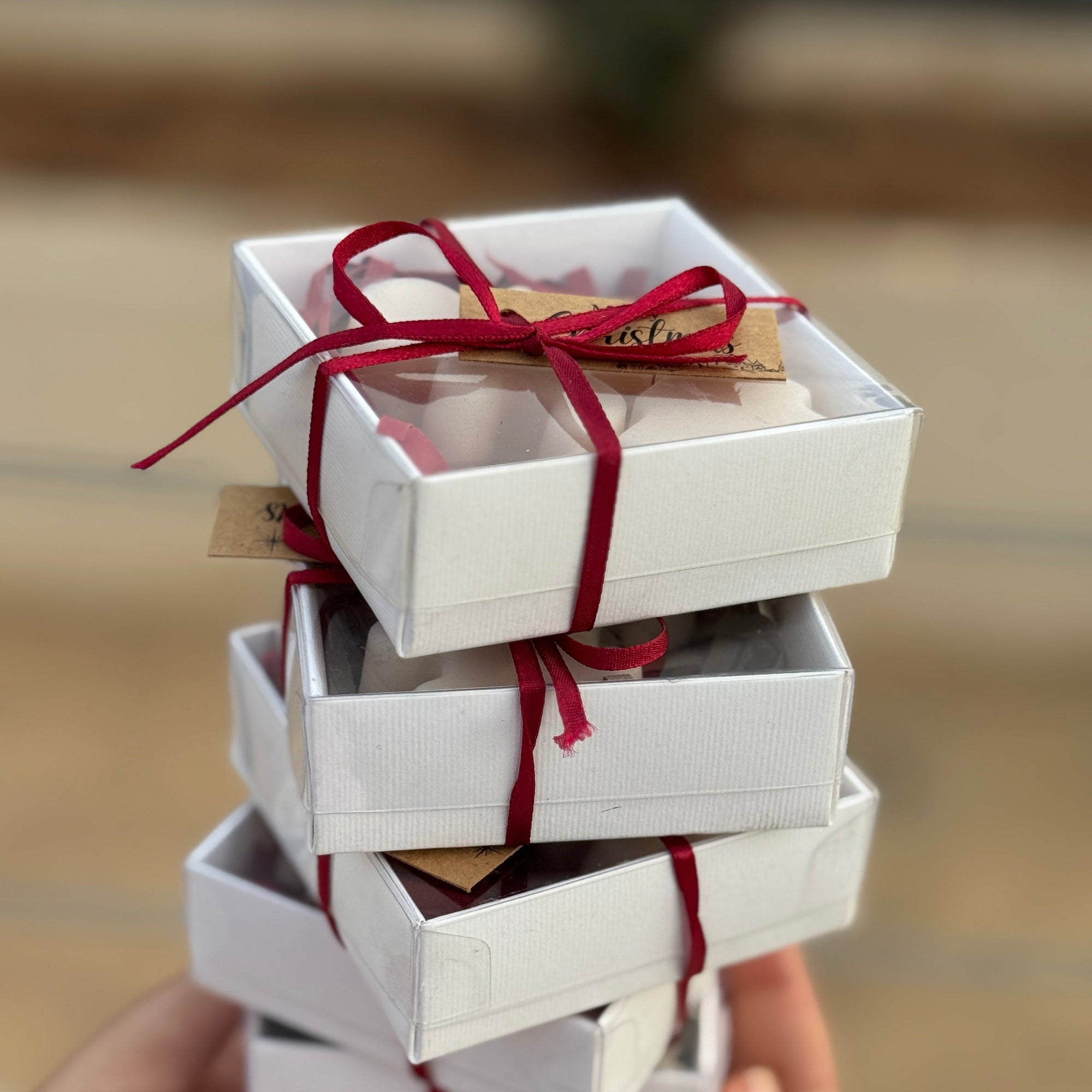 Stack of white Christmas gift boxes tied with red ribbons held by a hand against a blurred background